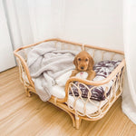 Handmade rattan pet bed with white blanket, maroon-pattern pillow, small dog resting