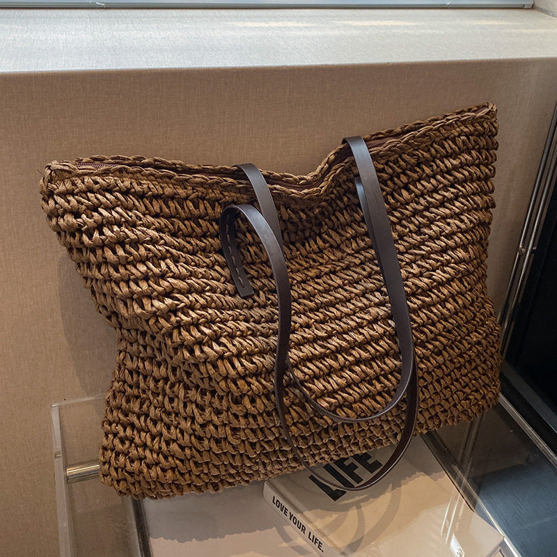 Woven shoulder beach bag in brown with dark handles and curved shoulder strap