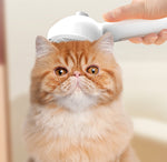 White mist grooming brush combing a light orange cat’s fur, handheld rounded head