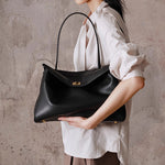 Black leather tote bag held by handles, front gold-tone clasp