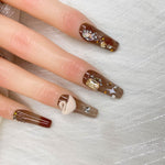 Short press-on nails close-up: brown gradient with nude and white bear, crystals, gold dots
