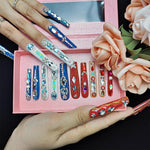Long press-on nails with blue base and rhinestone gems, outlined with silver studs