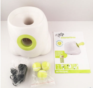 White dog ball launcher kit with lime-green chute, tennis balls, and power cord