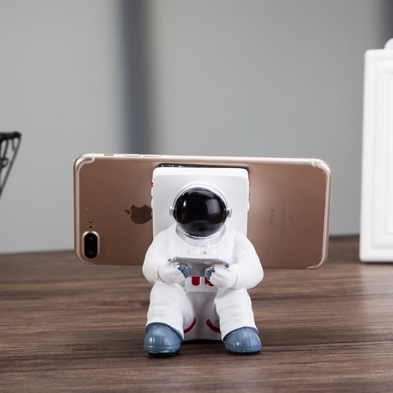 Astronaut resin phone stand showing smartphone back held by white spaceman figure