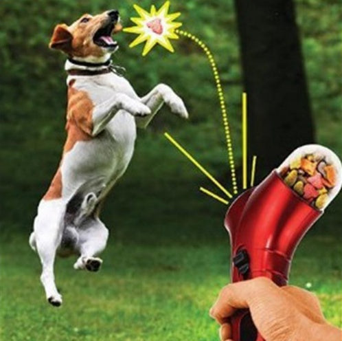 Red treat launcher toy held in a hand, open top for kibble, spring-loaded.