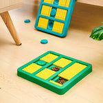 Green slow-feeding dog toy with yellow ridged compartments and teal paw lids