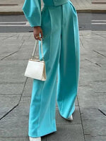 Teal high-waist wide-leg trousers with draped jacket sleeve and front crease
