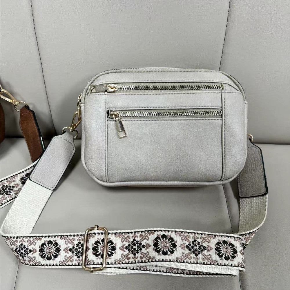 Light gray crossbody bag with front zippers and floral embroidered strap, gold-tone hardware