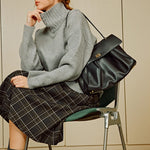 Black leather tote bag worn cross-body, with gold-tone front clasp detail