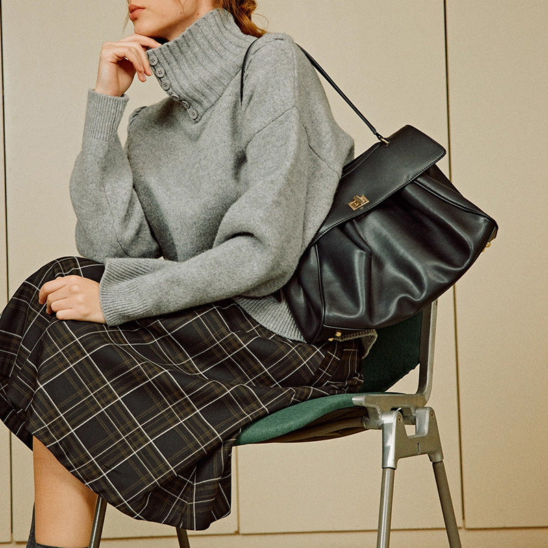 Black leather tote bag worn cross-body, with gold-tone front clasp detail