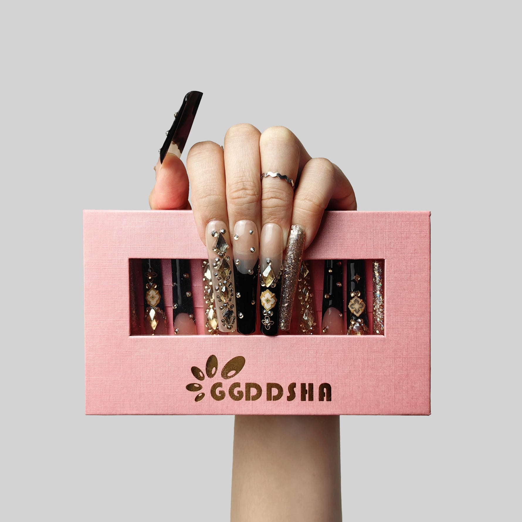 Hand wearing long press-on nails with nude base, black tips, and gold charm detailing