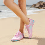 Pink water shoes with lace-up closure and teal-blue pattern accents on sand.