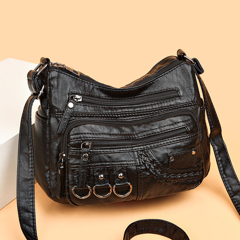 Dark PU leather crossbody bag with multiple zippers, braided pocket, and 3 ring accents