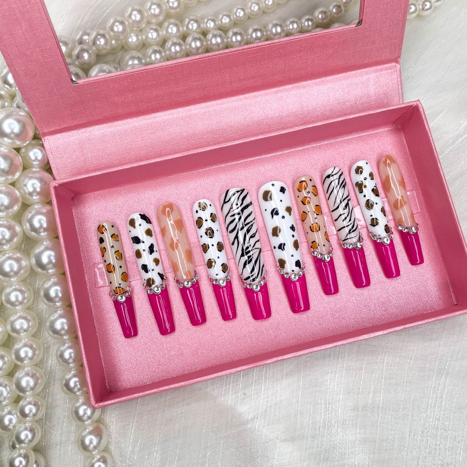 Stiletto press-on nails with zebra print, fuchsia tips, rhinestones, and charms
