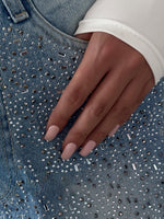 Blue denim pocket with rhinestone and bead-like embellishment; textured stitch lines