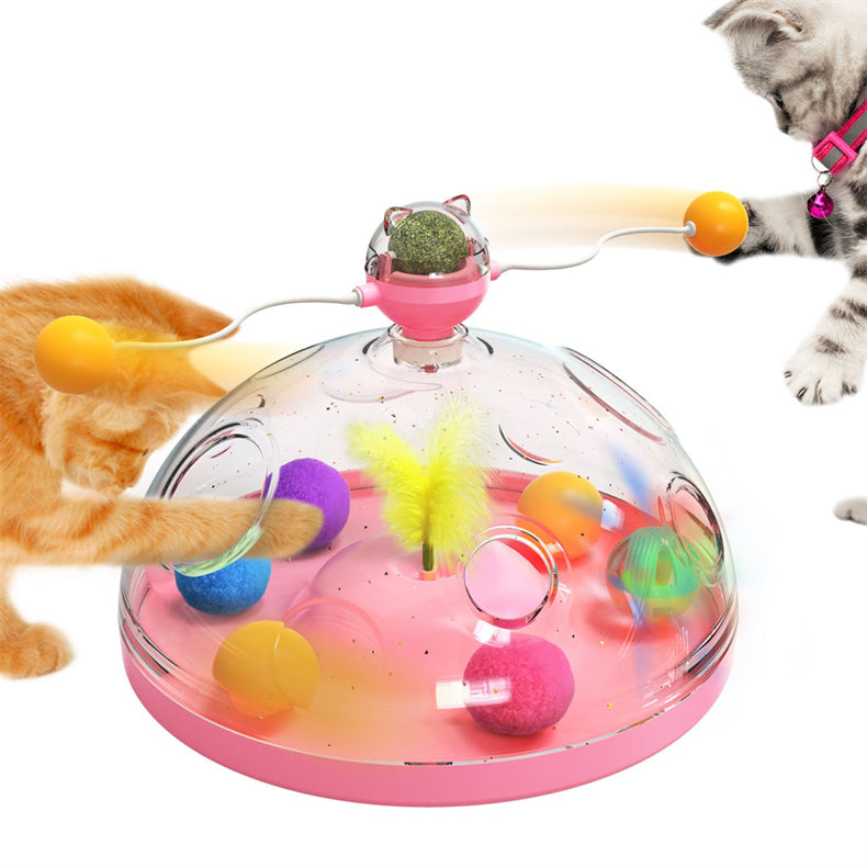 Interactive cat toy turntable with clear dome, pink base; orange cat reaching for dangling balls