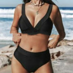 Black V-neck triangle bikini top and matching high-rise bikini bottoms on a beach.
