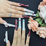 Long press-on nails on fingers, white snake pattern with red hearts and rhinestone accents