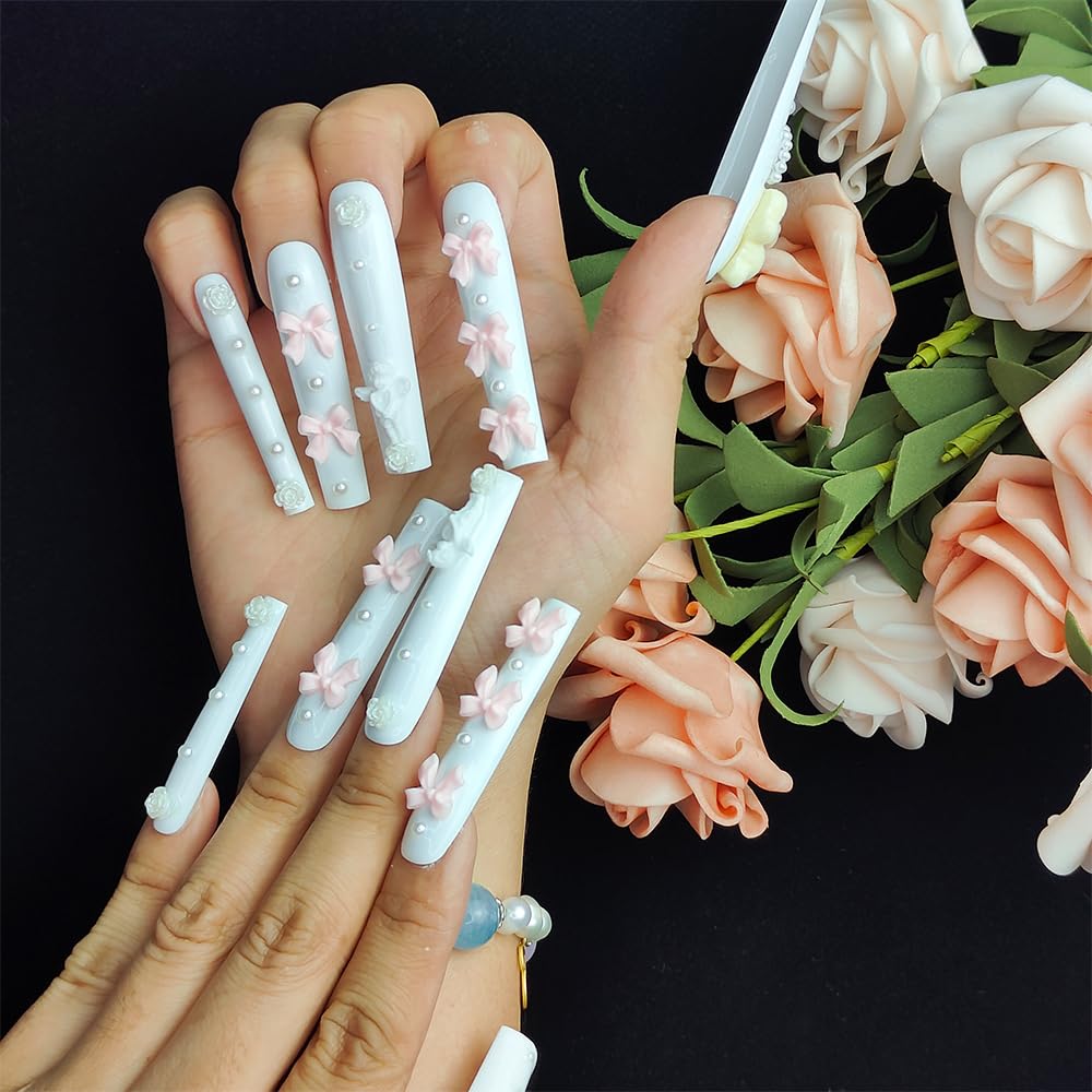 White press-on nails with pink bow charms and small bead dots, on a hand