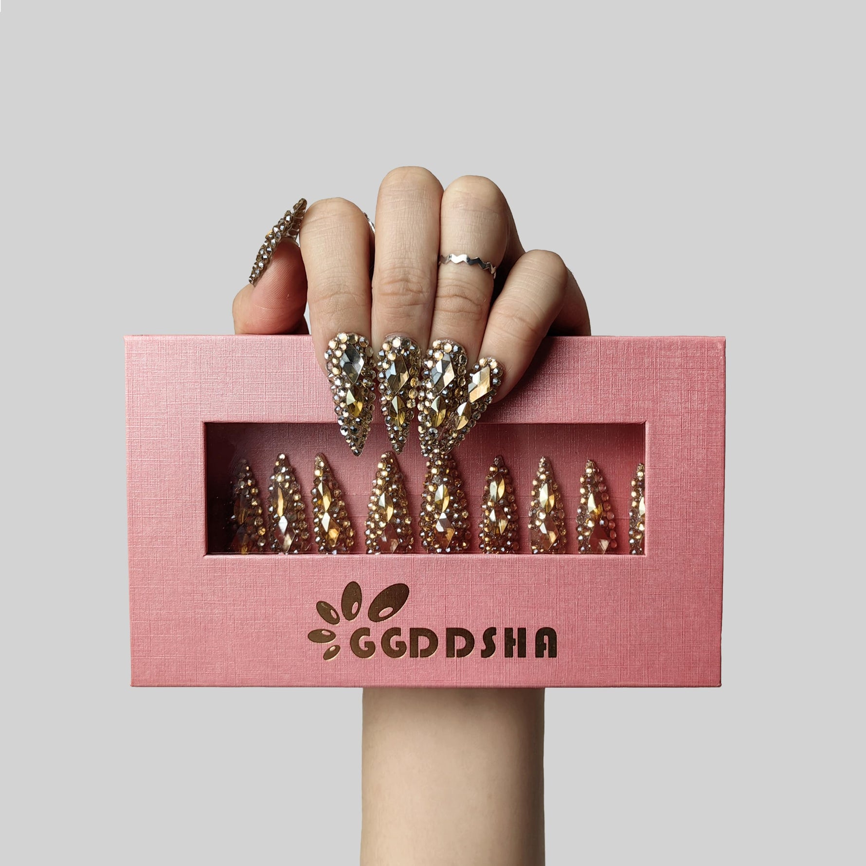 Almond press-on nails with gold and crystal rhinestone crown design in pink packaging