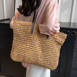 Woven shoulder beach bag in tan with black handles and adjustable shoulder strap