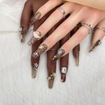 Short press-on nail set in brown and nude tones with gems, roses, and metallic details