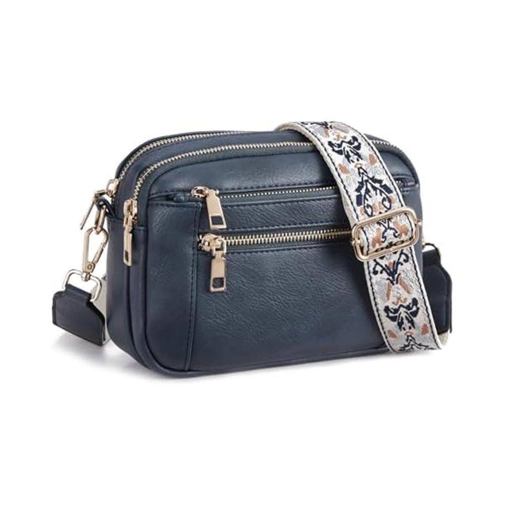 Navy blue crossbody bag with floral embroidered strap and gold-tone front zipper pockets