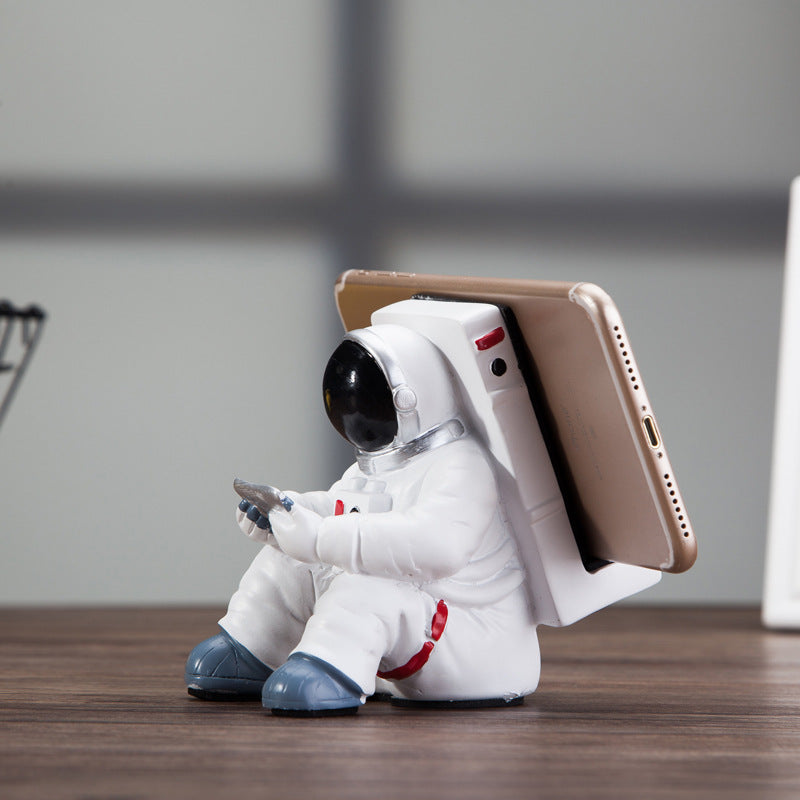 Astronaut resin phone stand with white spaceman figure holding a rose-gold smartphone