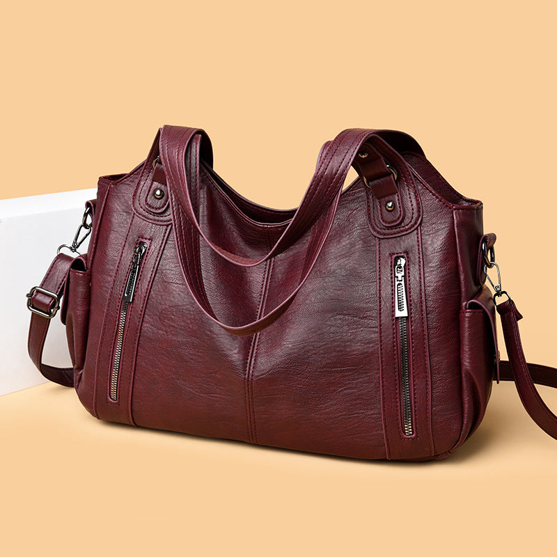 Burgundy PU handbag with top handles, shoulder strap, and front zip pockets