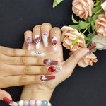 Long press-on nails on hands, red and white designs with silver detailing and rhinestones