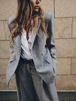 Light gray blazer with notch lapels and flap pocket, worn with wide-leg pants