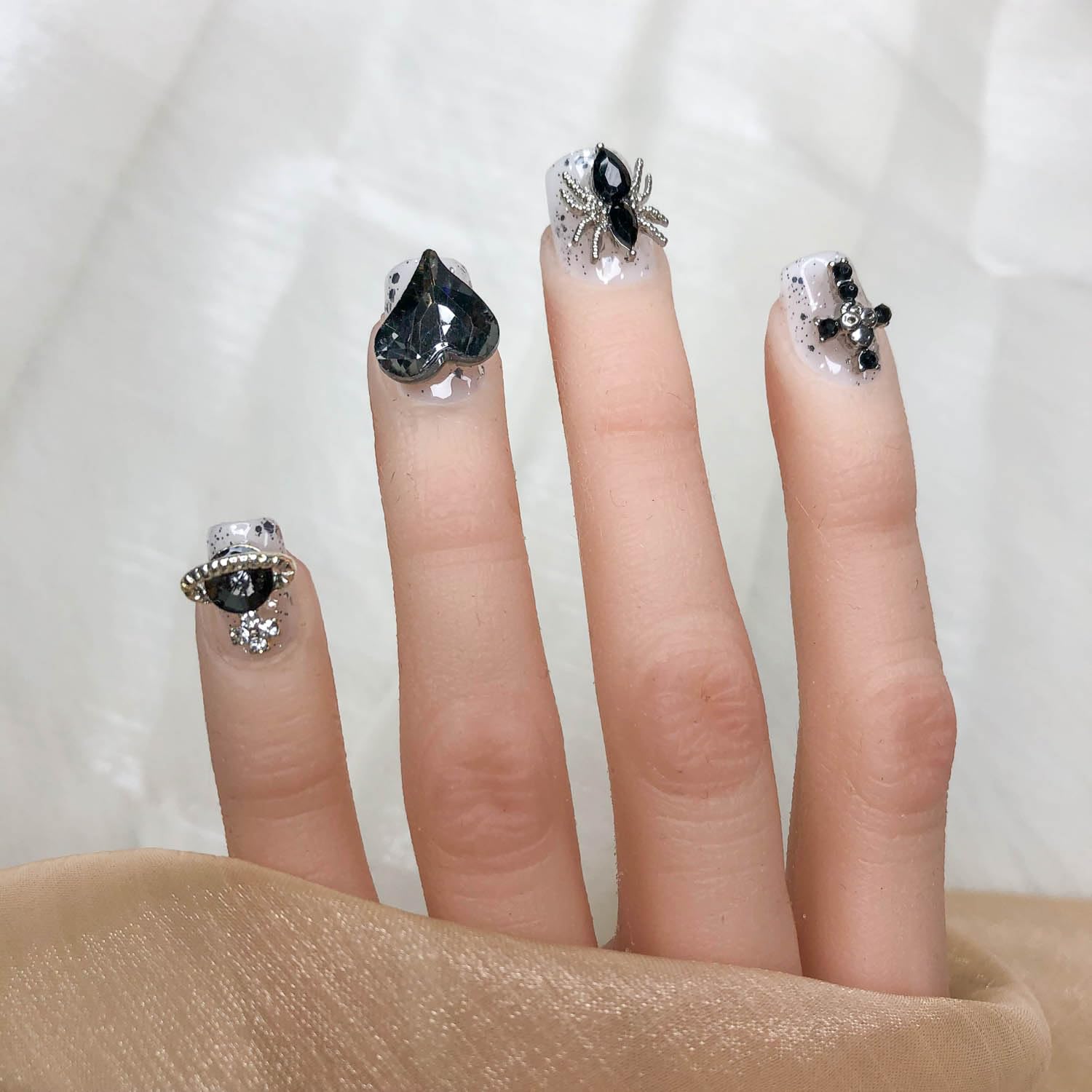 Short press-on nails with dark teardrop gems, silver glitter, and bow charms