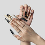 Long press-on nails set on hand: nude-and-black designs with gold gems and glitter nails