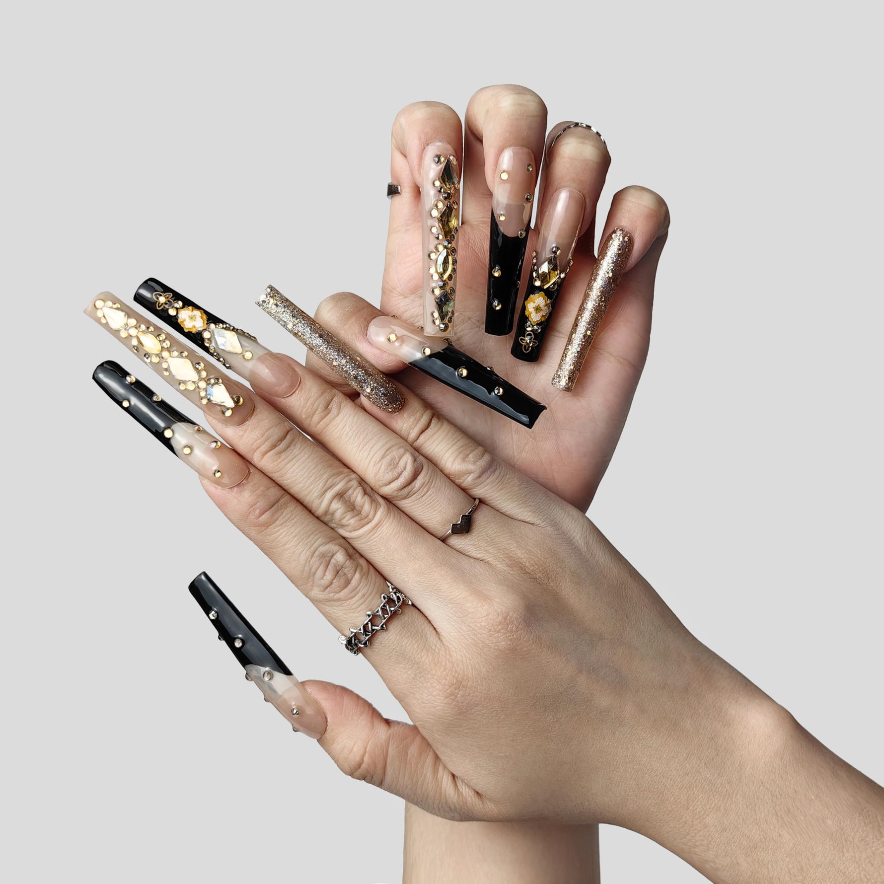 Long press-on nails set on hand: nude-and-black designs with gold gems and glitter nails