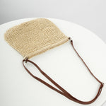 Woven straw crossbody tote with zipper closure and dark brown strap, laid flat