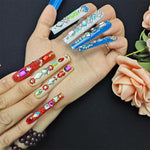 Long press-on nails on hand: red, blue, green and purple gem designs with glossy shine