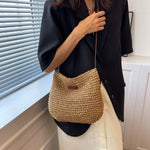 Woven straw shoulder tote with dark brown trim and short strap, worn with dark top