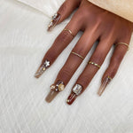 Short press-on nails in deep brown with nude tips; star charms and a red gem accent