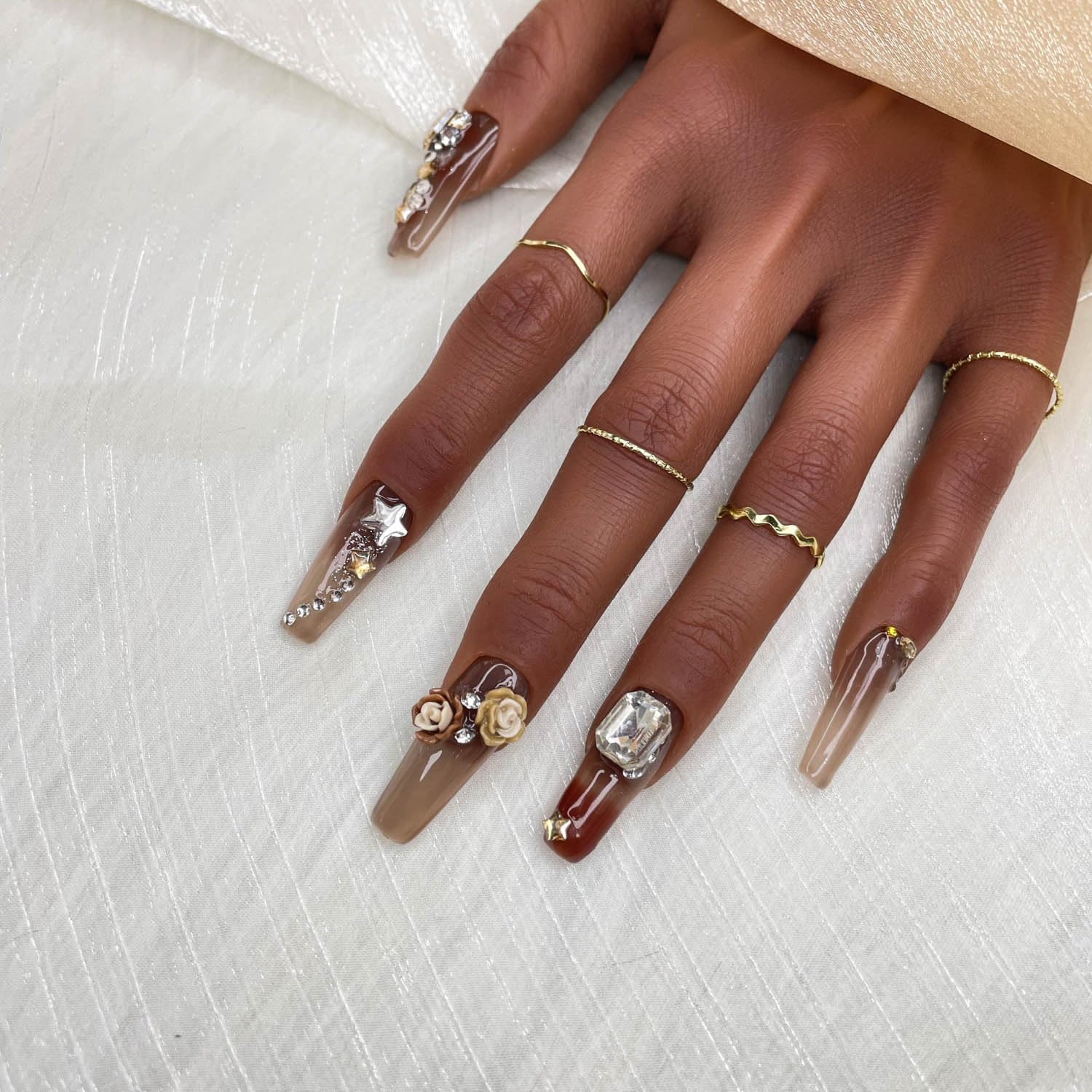 Short press-on nails in deep brown with nude tips; star charms and a red gem accent