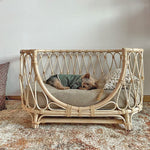 Handmade rattan pet bed with gray cushion, patterned pillows, white woven sides