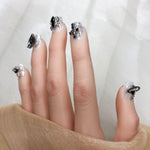 Short press-on nails with black jewel accents, silver speckled base, rhinestone bow details