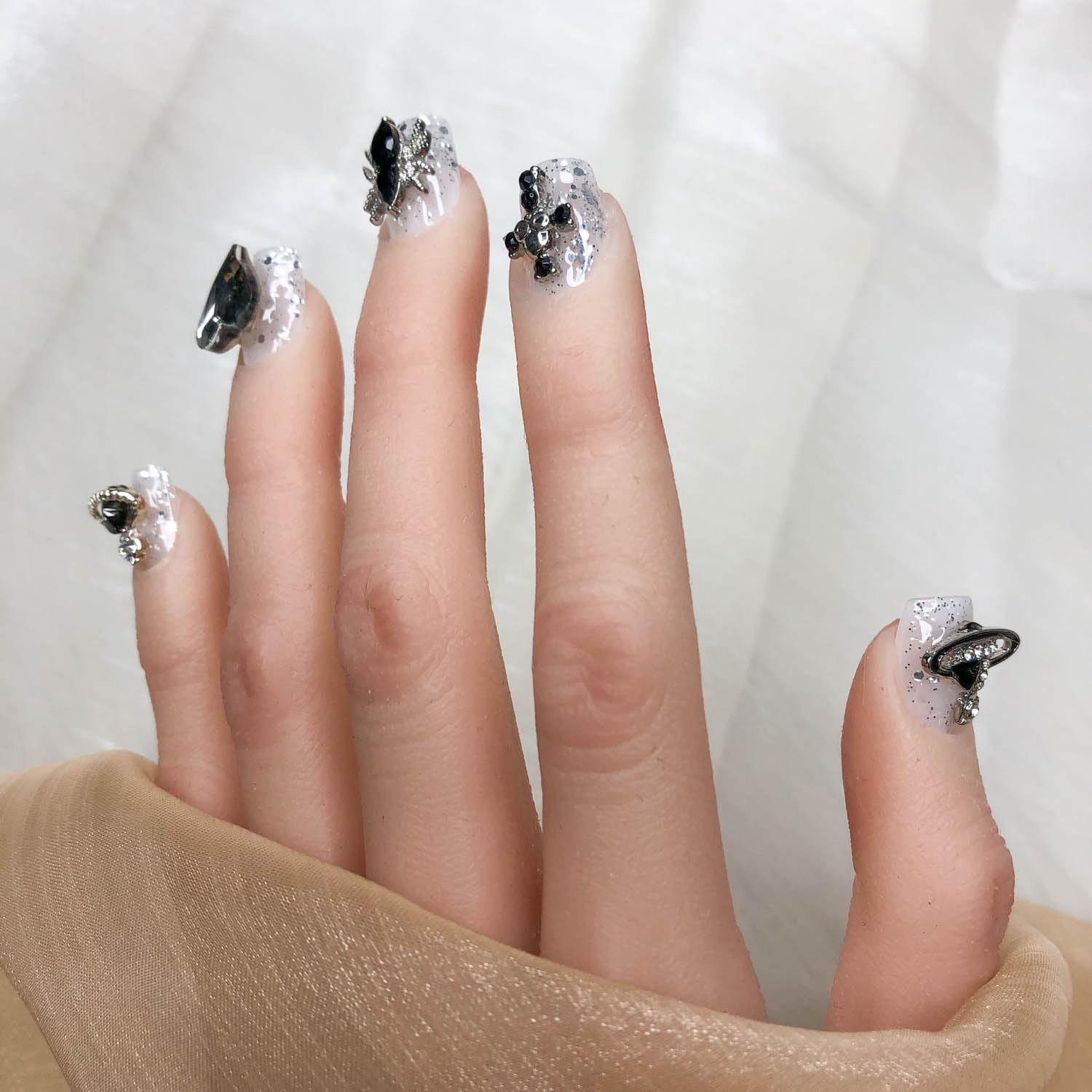 Short press-on nails with black jewel accents, silver speckled base, rhinestone bow details