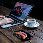 Black wireless charging pad with a smartphone resting on top beside a laptop