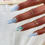 Long square press-on nails with blue base, silver glitter edges, and emerald green gem