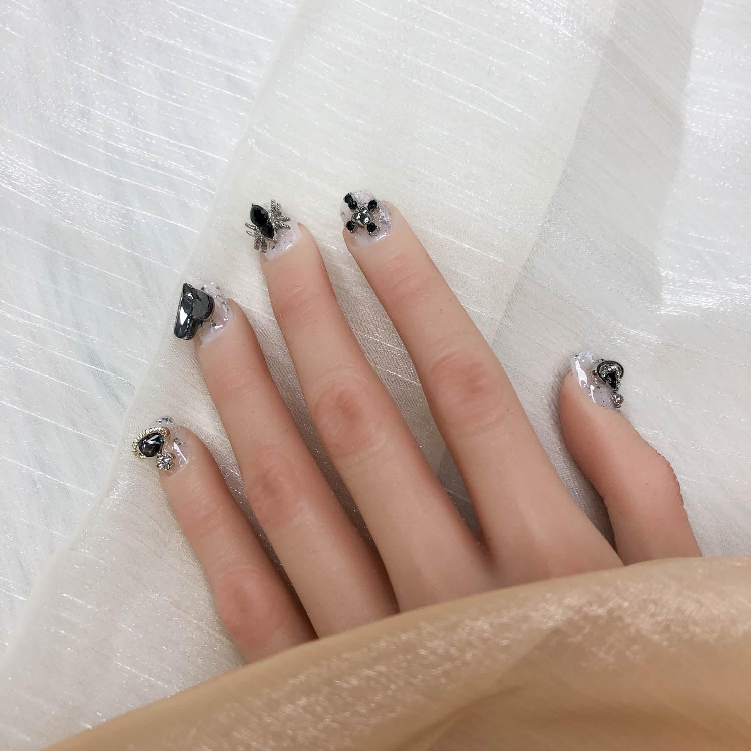 Short press-on nails with black gem bow and bead embellishments on silver glitter