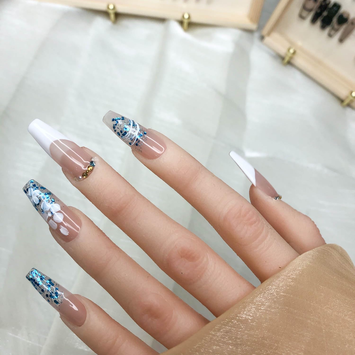Short press on nails, nude pink gradient with blue glitter, white flowers, and gold embellishments