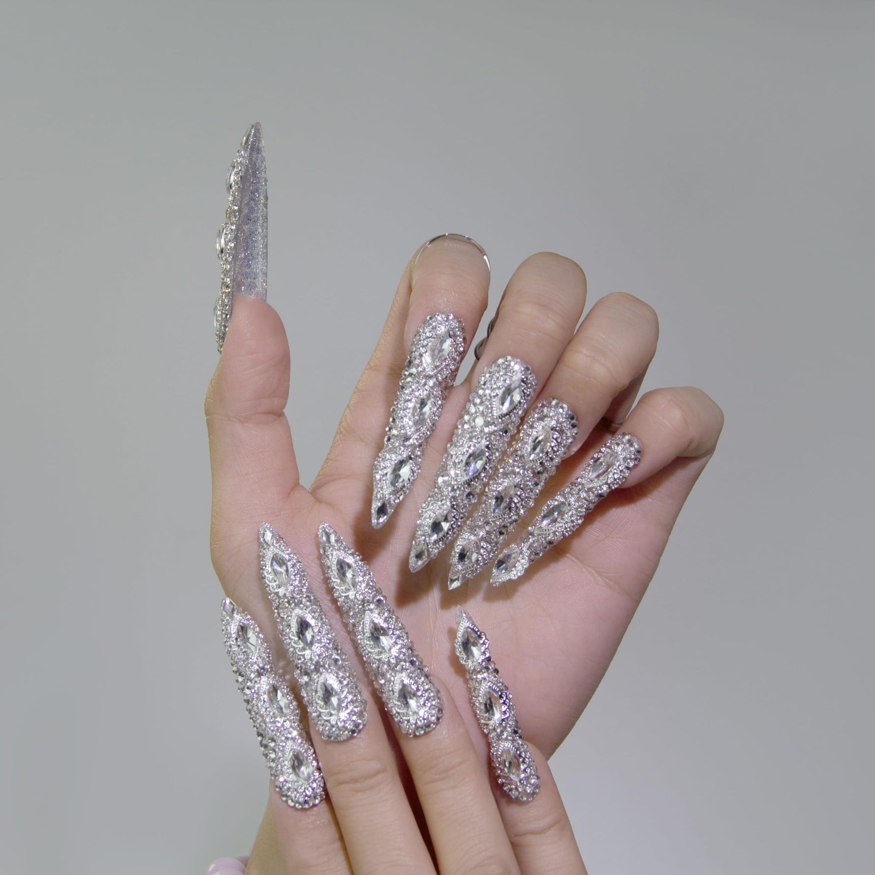 Hand wearing long almond silver rhinestone press-on nails with 3D crystal detailing