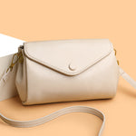 Beige-white PU crossbody bag with flap front, circular snap, and crossbody strap