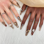 Short press-on nails with glossy brown gradient, nude, and white accents plus gems and stars