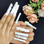 Light blue press-on nails with bow and pearl charms, shown on a hand